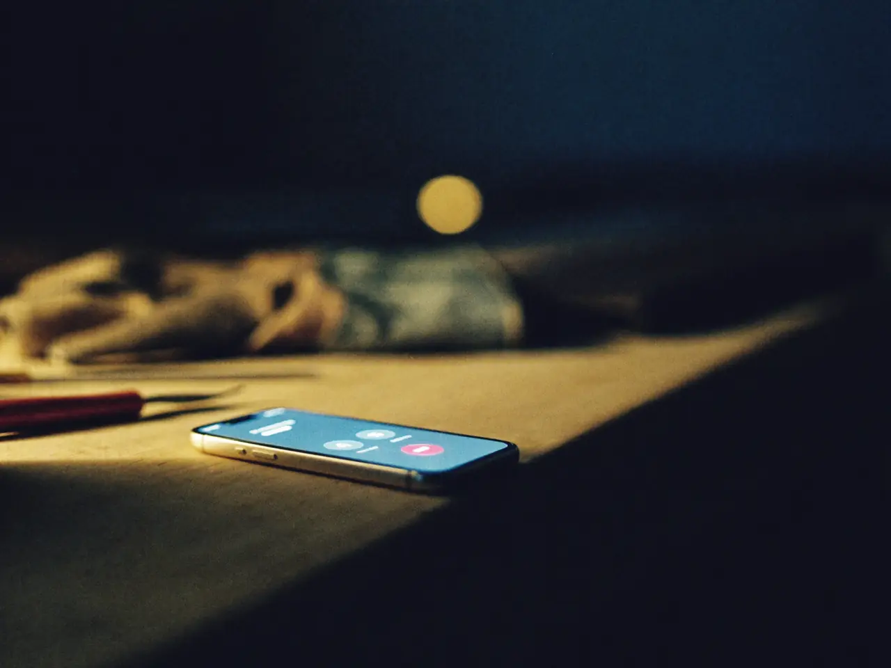 Celular sobre una mesa de trabajo de noche, con una llamada entrante iluminando la pantalla